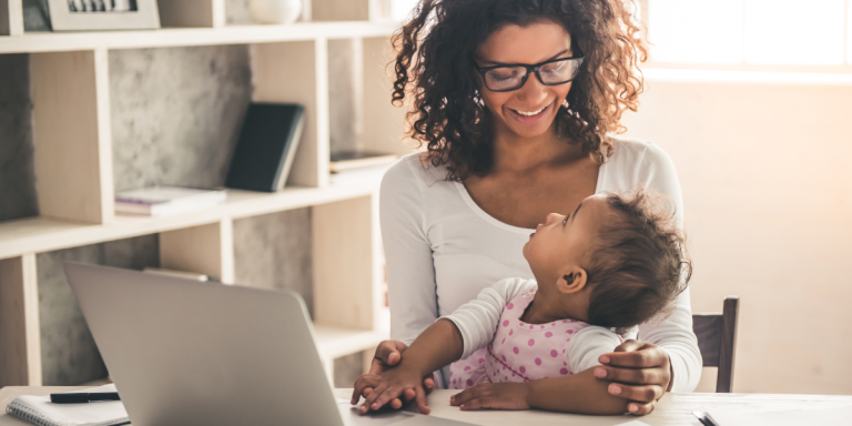 Working mum enjoying her time at home with her child A mother holds her young child while working on a laptop at home as part of her guide to returning to work after maternity leave