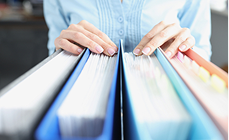 Hands selecting a ring binder from a row of colourful financial records folders Hands selecting a ring binder from a row of colourful financial records folders