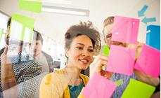 Smiling woman planning a new business with colourful sticky notes on a glass wall Smiling woman planning a new business with colourful sticky notes on a glass wall