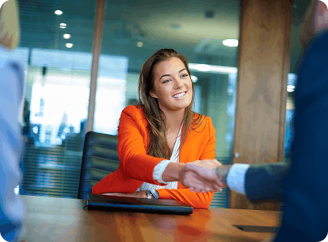 New employee in an orange blazer shaking hands with her employer after a job interview