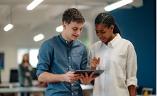 Two colleagues reviewing information on a tablet in an open plan office Two colleagues reviewing information on a tablet in an open plan office