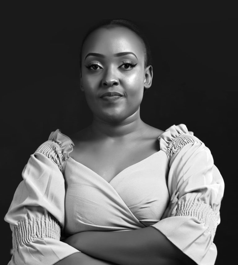 Tonia Kimani, Pitman Training Kenya Administrative Assistant Diploma graduate, seated with arms crossed in a black and white portrait